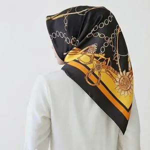 Black and gold satin square scarf with chain sun pattern worn as a chic headscarf