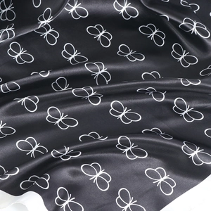 Detailed view of black satin fabric with elegant white butterfly outlines and silky texture