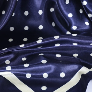 Detail of navy blue satin silk scarf with white polka dot pattern and smooth texture