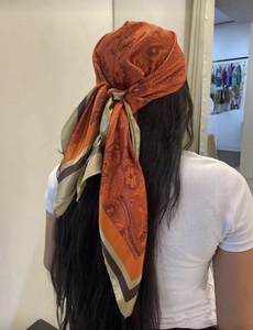 Detail of satin paisley scarf worn as a hair wrap in orange and beige tones