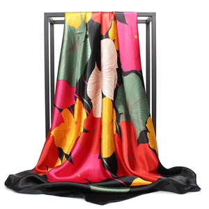 Silk satin scarf with vibrant floral leaf prints displayed on a black metal rack