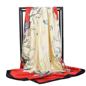 Detailed view of elegant bird and floral prints on a satin scarf with red borders