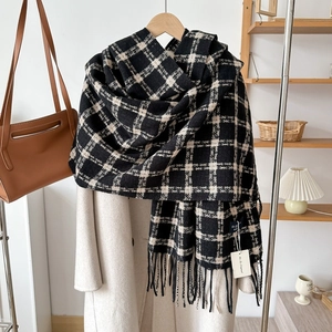 Detail of soft black and white plaid scarf with long tassels on a beige coat