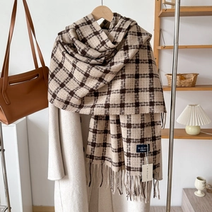 Plaid cashmere-like winter scarf with tassels on a wooden hanger with a beige coat