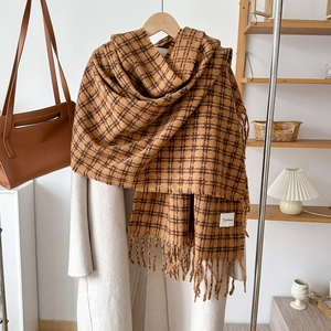 Caramel plaid cashmere scarf detail with tassel edges styled on a wooden hanger