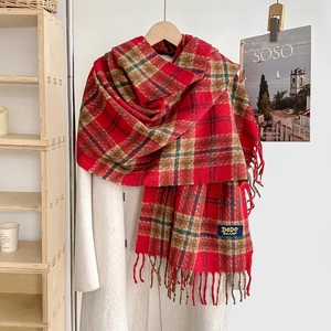 Détail d'une écharpe à carreaux rouge et marron avec franges sur un manteau beige