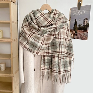 Soft plaid scarf in forest green and warm brown with decorative tassels on a beige coat