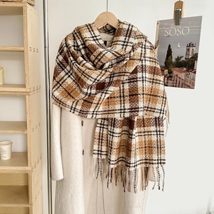 Detail of soft plaid scarf with tassels in caramel and beige tones styled on a coat