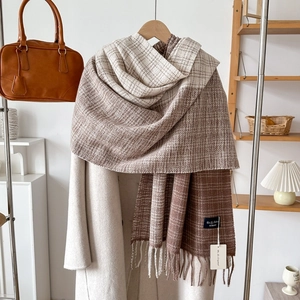 Detail of thick brown and beige plaid knit scarf with long tassels on beige coat