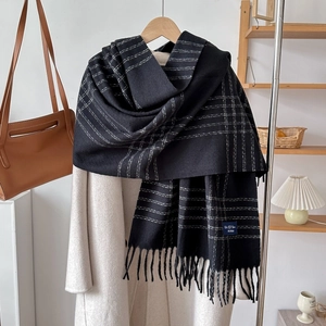 Close-up of black and white checkered scarf with long tassels on a beige coat