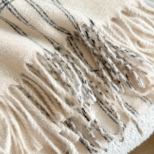 Macro shot of cream knit shawl with black stripes and decorative long fringe detail