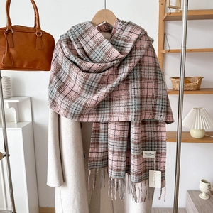 Pink and blue plaid cashmere-like scarf with tassels hanging on a beige wool coat
