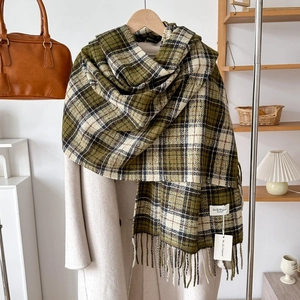 Detail of green plaid cashmere scarf with soft tassels and brand label on a wooden hanger