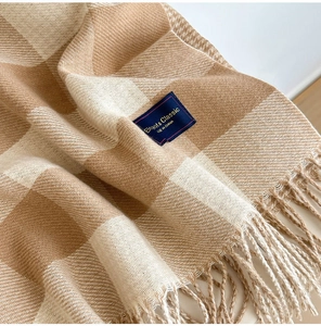 Close-up of beige plaid scarf showing soft knit texture, tassels, and elegant woven label