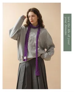Detail of a purple narrow knit scarf with a white woven label on a grey sweatshirt