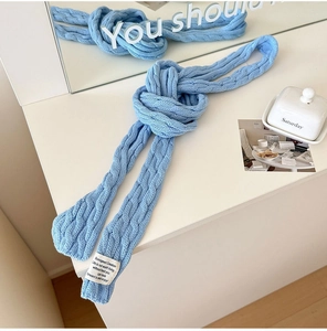Close-up of light blue cable knit scarf with a decorative brand label on a white desk