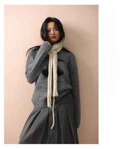Detail of slim off-white knitted wool scarf paired with a grey cherry knit sweater