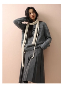 Detail of a thin beige knitted wool scarf paired with a grey sweater and pleated skirt