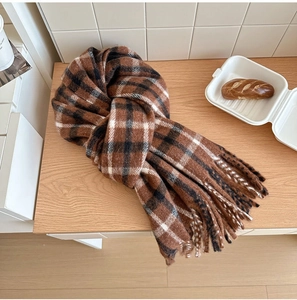 Détail de l'écharpe en laine à carreaux marron et noir avec des franges sur bois