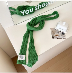 Macro detail of green cable knit scarf with a white woven label on a vanity desk