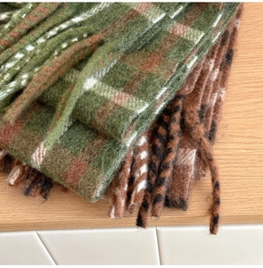Gros plan d'une écharpe en laine à carreaux épais avec des franges vertes et brunes