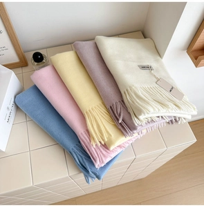 Close-up of soft wool scarves with fringe in pastel colors on a stylish tiled surface