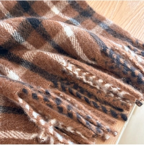 Détail macro de l'écharpe épaisse en laine à carreaux avec franges et texture douce