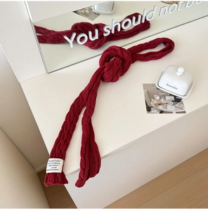 Detail of dark red knit scarf showing fine cable knit texture and white fabric label