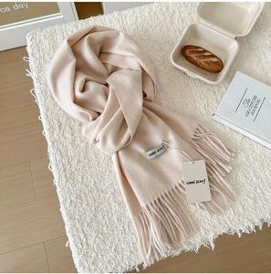 Detailed close-up of apricot wool scarf with soft fringe tassels and authentic woven label