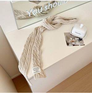 Detail showing the cream cable knit texture and fabric label on the narrow stylish scarf