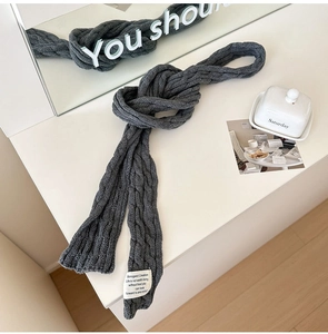 Close-up of thick dark grey cable knit scarf with a minimalist white lifestyle label