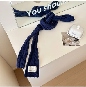 Macro shot of navy blue cable-knit scarf showing detailed texture and white woven label