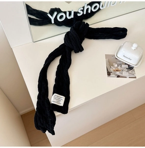 Detail of black knit scarf with vertical stripes and woven label on a white surface