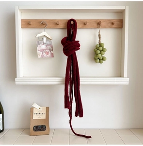 Detail of dark red knit wool scarf showing rich texture hanging on a wooden hook