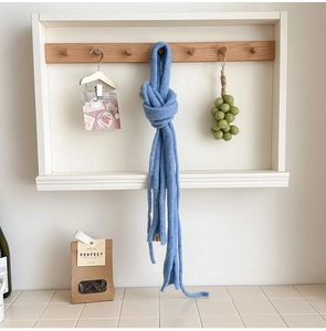 Close-up of light blue knitted wool scarf hanging on a wooden hook in a cozy home setting