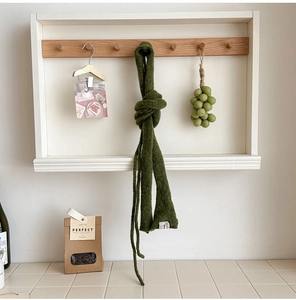 Detail of a dark moss green knit scarf with a white brand label on a wooden hook