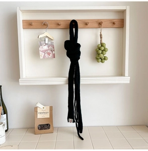 Detail of slim black knit scarf with small red-white brand label hanging on wooden hook