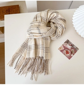 Detail shot of a cream plaid cashmere-like scarf with thin black lines and soft tassels