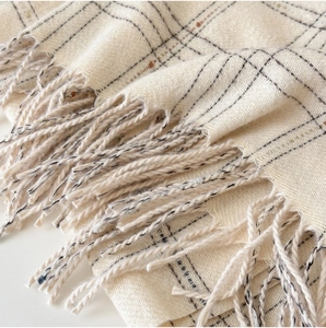 Close-up of fringe details and soft plaid weave texture on a cream cashmere-like scarf