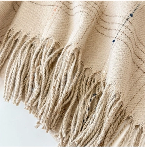Macro detail of beige cashmere-like scarf showing soft plaid fabric and knotted tassels