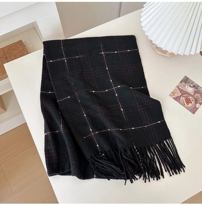 Close-up of black plaid cashmere scarf with gold lines and soft fringe on table