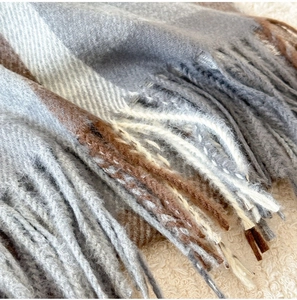 Close-up of classic grey plaid scarf with soft fringe on warm fleece background