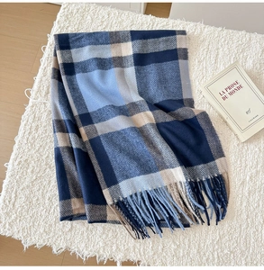 Detailed view of classic blue and beige plaid scarf with fringe on soft plush surface