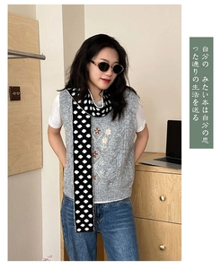 Close-up of gray knit vest with floral embroidery and black and white polka dot scarf
