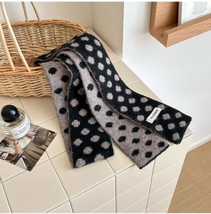Detailed close-up of soft knitted polka dot scarf with brand label on a tiled surface