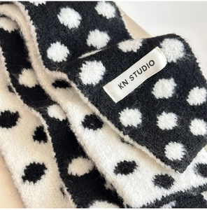 Close-up of soft knitted scarf with black and white polka dots and KN STUDIO label