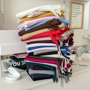 Stack of colorful solid wool scarves with tassels in minimalist home setting