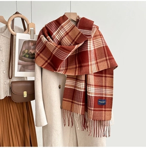 Détail d'une écharpe à carreaux rouge et orange avec pompons sur un manteau beige