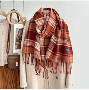 Détail d'une écharpe à carreaux rouge et orange avec pompons sur un manteau beige