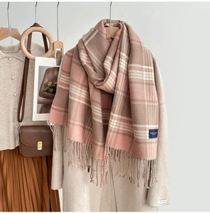 Détail d'une écharpe à carreaux doux avec franges roses et beige sur cintre